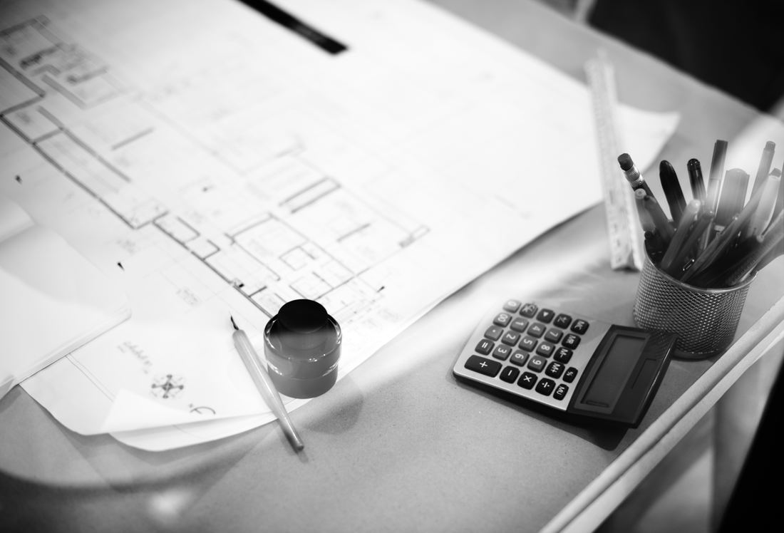 A black and white image of a calculator and pens sitting on house plans