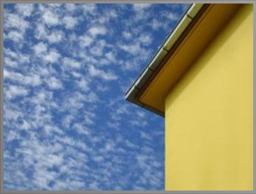 A  new gutter has been installed on a yellow-painted home against a blue sky backdrop